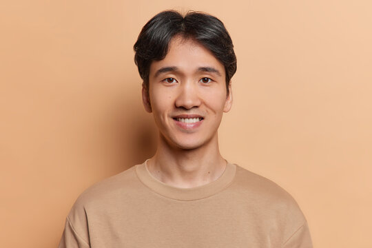 Portrait of handsome dark haired man smiles positively dressed in casual t shirt being satisfied with good news wears casual t shirt isolated over brown background. People and emotions concept