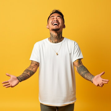 adult tattooed Asian man in white t-shirt shows his hands to the side on yellow isolated background and smiles 