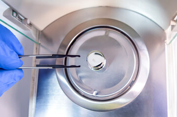 A operator's hand is holding steel calibration weight to place on the analytical balance. Concept...