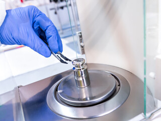 A operator's hand is holding steel calibration weight to place on the analytical balance. Concept of quality control in a laboratory.