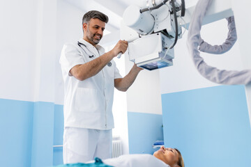 A diverse team of radiologists, along with a young female patient, gathers in the X-ray room. One...
