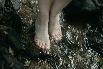 A girl stands barefoot in a mountain stream. Women's legs close-up in the water.