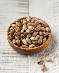 Dried pistachio nuts in a wooden bowl on a white wooden background. Healthy eating, nuts.