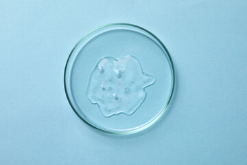 Petri dish with sample of cosmetic oil on light blue background, top view