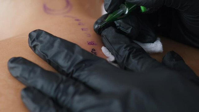 Tattooing process. Close up. Tattoo machine studio female artist. Black gloves.