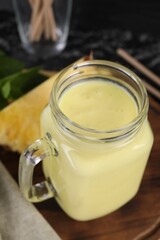 Tasty pineapple smoothie in mason jar on table, closeup