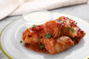 Delicious stuffed cabbage rolls cooked with tomato sauce and sour cream on table, closeup