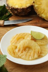 Tasty grilled pineapple slices and piece of lime on wooden table, closeup