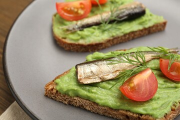Delicious sandwiches with sprats, tomatoes, avocado puree and dill on wooden table, closeup