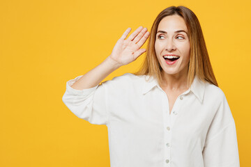 Young curious nosy caucasian fun happy woman she wearing white shirt casual clothes try to hear you overhear listening intently isolated on plain yellow background studio portrait. Lifestyle concept.