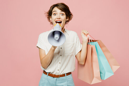 Young amazed woman wear casual clothes hold shopping paper package bags scream in megaphone announces discounts sale Hurry up isolated on plain pink color background Black Friday sale buy day concept