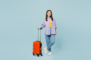 Traveler happy woman wear casual clothes hold suitcase bag look camera isolated on plain pastel blue background. Tourist travel abroad in free spare time rest getaway. Air flight trip journey concept.