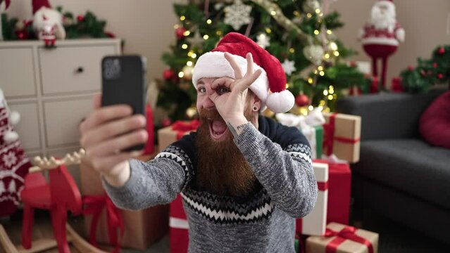 Young redhead man make selfie by smartphone sitting on floor by christmas tree at home