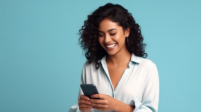 Young adult smiling happy pretty latin woman holding mobile phone looking at smartphone, typing message doing ecommerce shopping on cell, using trendy apps on cellphone isolated on blue background 