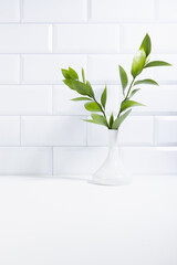 Summer bathroom interior with green tropical bouquet in vase in sunlight, white tiled wall, wood shelf, copy space. Spring interior background for presentation cosmetic products, advertising, design.