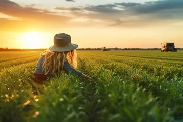 Foto op Plexiglas Young woman farmer weeding grass on wheat farm in background of blurred wheat farm on tractor with beautiful sunset sky. Production concept of agriculture and farmers. © cwa