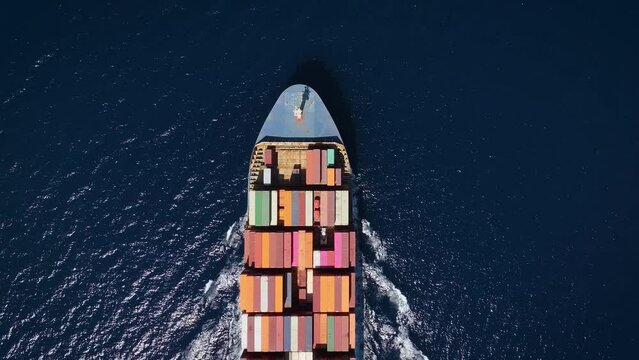 Aerial top down view of a bow from a large container cargo ship traveling with speed over blue ocean