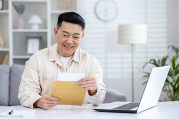 Happy and successful asian received mail notification envelope with good news, man sitting at table...