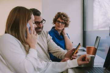 Good looking 50s businessman showing something funny on the phone to his blonde female colleague while she is having a phone call