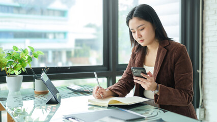 Beautiful asian businesswoman sitting at her workplace and using smart phone.