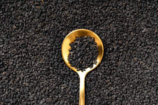 Black cumin seeds on golden spoon for production of black cumin oil