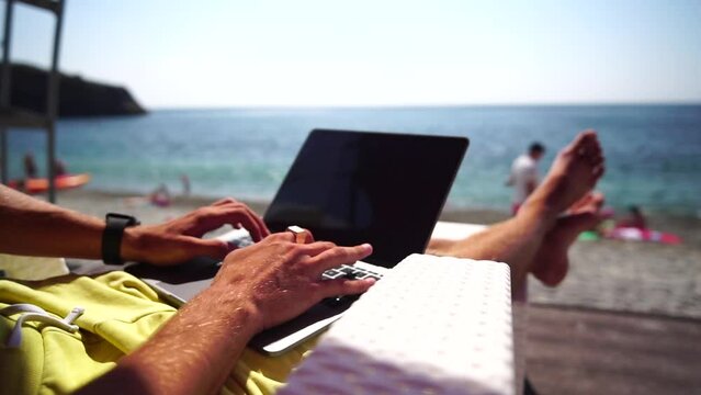 Man laptop sea. Working remotely on seashore. Happy successful man, male freelancer working on laptop on beach, relieves stress from work to restore life balance. Freelance, remote work on vacation