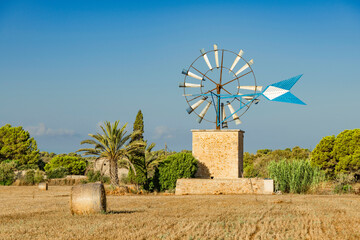 Typical Majorcan rural landscape
with windmill of a water pump for irrigation and bales of straw on a harvested field - 7453