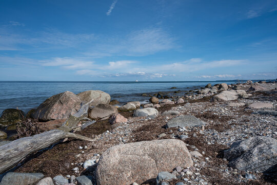K&uuml;stenline an der Ostsee, sehr Steinig aber auch Holz ist hier zu finden. Dahinter liegt friedlich die Ostsee. Ein sch&ouml;ner Himmel rundet das Bild ab