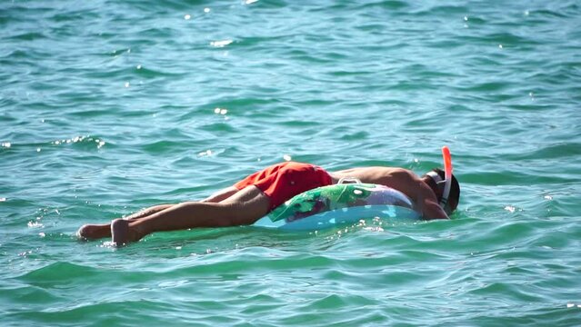 Summer Vacation man in diving mask floats on inflatable donut mattress, water toy swim ring. Positive happy man relaxing and enjoying family summer travel holidays vacation on the sea. Slow motion