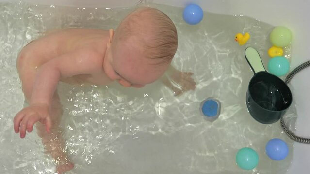 The cheerful child is having fun in the bathtub with some toys. Slow motion of a cute toddler boy enjoys his bath time.