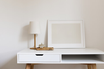 Blank horizontal  frame mockup on the white table with the minimalistic table lamp and wooden tray with a silver decorative pumpkin. Modern interior design, home, office desktop.