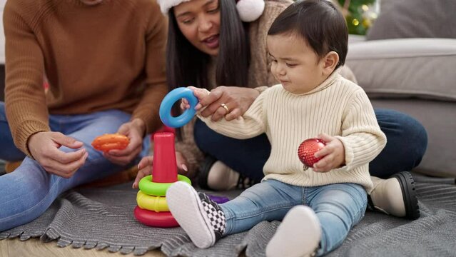 Couple and son sitting on floor by christmas tree playing with hoops toy at home