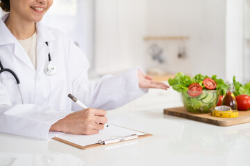 Woman dietitian in medical uniform with stethoscope working on a diet plan sitting with different healthy food ingredients in  office on background. Weight loss and right nutrition concept