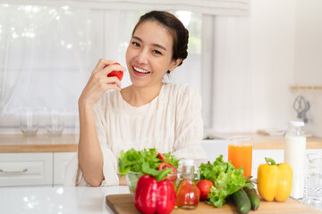 Obraz na płótnie Canvas Healthy food is healthy life. beautiful young asian woman holding fresh red tomato and smiling with vegetable salad on table in the kitchen