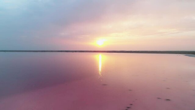 Aerial of a sunset at pink lake Bursol. Drone flying above calm surface of the lake with reflections of sun. Salt mining in Altai region of Russia