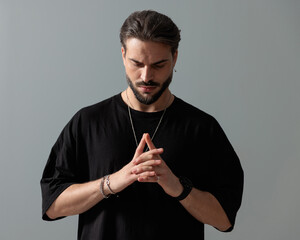 fashion young man with beard holding hands together and looking down