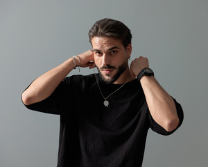 sexy young man with beard adjusting necklace and looking forward