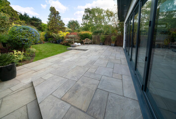 Beautiful indian sandstone patio with attractive garden and bifold doors. - obrazy, fototapety, plakaty