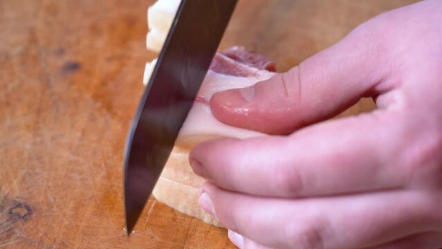 Slicing of salted pork fatback on cutting board, close-up. Ukrainian traditional food - salo	
