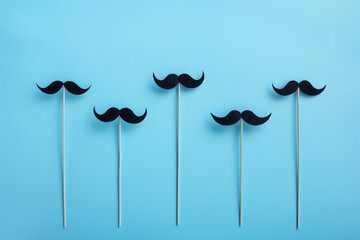 movember concept, black mustaches with sticks on a blue background - obrazy, fototapety, plakaty