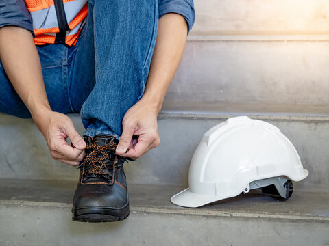 Male worker hands tying shoelaces on leather safety shoes with white protective helmet or hard hat on concrete stair in construction site. Safety workwear for worker and foreman