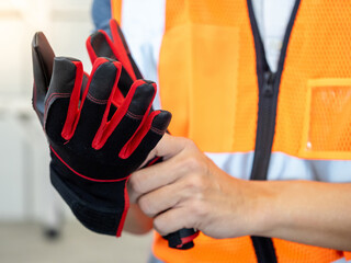 Male construction worker with reflective orange vest putting black and red protective gloves on his...