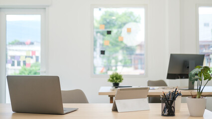 Bright modern office with computer laptop, houseplant and supplies on wooden table.