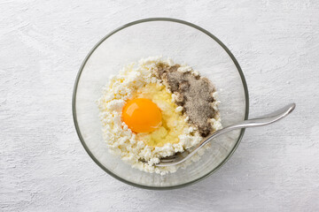 Glass bowl with cottage cheese, egg and vanilla sugar on a light gray background, top view. Cooking stage