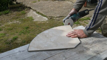 sanding the edge of a large decorative light tile in an outdoor workshop using a round sanding attachment, processing building finishing material with an angle saw with sandpaper - obrazy, fototapety, plakaty