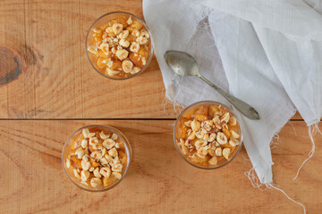 Three glasses with apples and hazelnuts pastry from above. At side: a spoon and a white linen napkin.