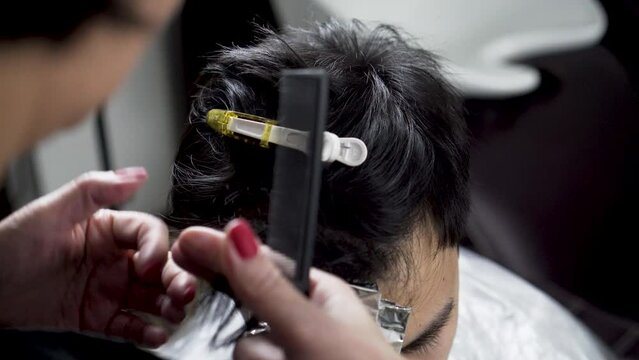 Closeup of hands with scissors and comb making haircut to a person