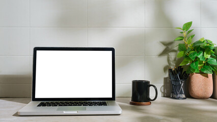 Minimal workplace with laptop computer, coffee cup, pencil holder on white table.