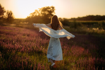Happy relaxed woman dancing in a field of lilac wildflowers at sunset, concept of dreams, freedom...