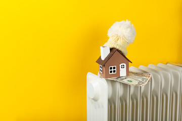 Home heating radiator. A model of a house wrapped in a scarf and a hat on a radiator indoors...